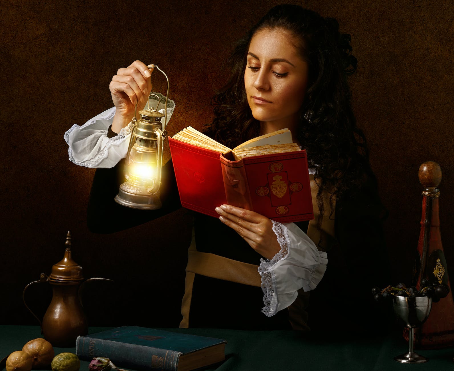 focused woman in old outfit reading book with oil lamp